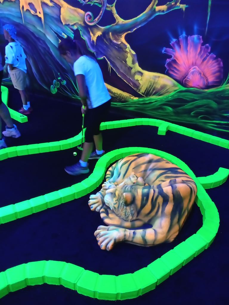 Un enfant joue au mini-golf devant le tigre fluorescent